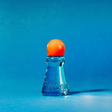 A small clear blue glass bottle or vial with a rounded orange cap, photographed on a smooth blue studio background.