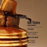 A close-up of a stack of pancakes topped with thick caramel sauce and a vanilla bean, next to text reading 'the Notes CARAMELT' and scent notes 'ON SKIN' and 'MELT IN SKIN'.