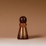 A frosted amber glass perfume bottle with a dark brown spherical cap, featuring the brand name 'Knock' embossed on the front, set against a solid warm brown background.