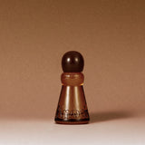 A frosted amber glass perfume bottle with a dark brown spherical cap, featuring the brand name 'Knock' embossed on the front, set against a solid warm brown background.