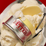 A jar of FIRMING BODY BUTTER SEOUL VANILLA sits atop vanilla ice cream, providing deep moisture for smooth skin, with a yellow spatula and a vanilla bean next to it, all set against a bold red background.