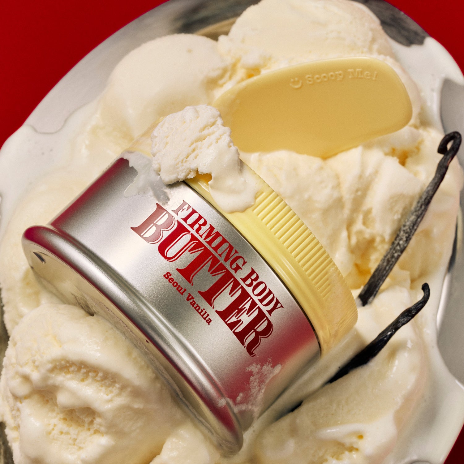 A jar of FIRMING BODY BUTTER SEOUL VANILLA sits atop vanilla ice cream, providing deep moisture for smooth skin, with a yellow spatula and a vanilla bean next to it, all set against a bold red background.