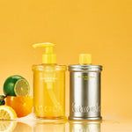 Two bottles, one with a pump and one metallic, on a yellow background with citrus fruits.